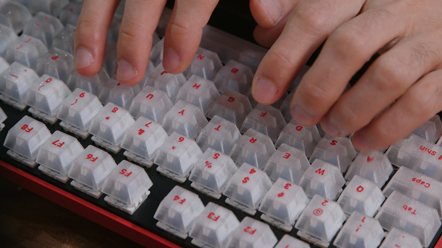Hände tippen auf einer rot-schwarzen mechanischen Tastatur mit weißen Tasten.
